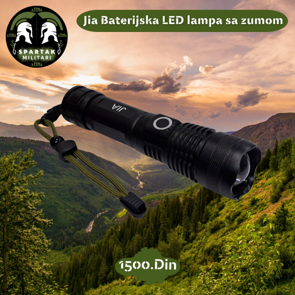 Jia LED baterijska lampa sa kaišem za ruku, položena na planinskom pejzažu pri zalasku sunca.